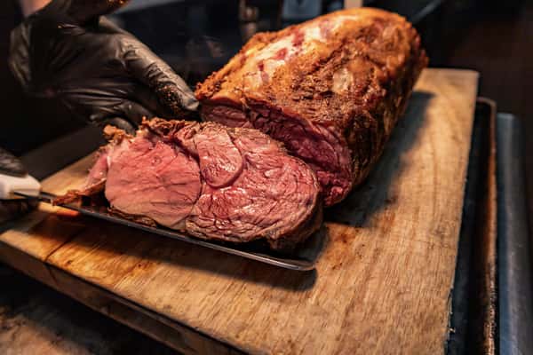 Close-up of a juicy, medium-rare prime rib roast being hand-carved on a wooden cutting board, showcasing tender, marbled beef with a crisp outer crust.