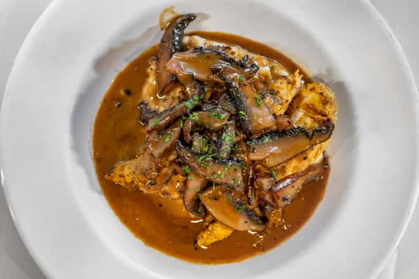 Grilled chicken breast smothered in savory mushroom gravy with sliced portobello mushrooms, served over mashed potatoes in a white bowl.