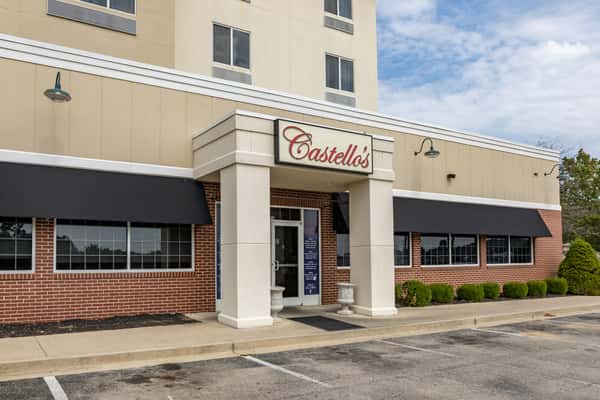 Exterior of Castello's restaurant featuring brick and tan siding, large black awnings, and a front entrance with white pillars under a red and white sign.
