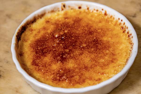 Classic crème brûlée with a perfectly caramelized sugar crust in a white ramekin, showcasing its rich golden texture.