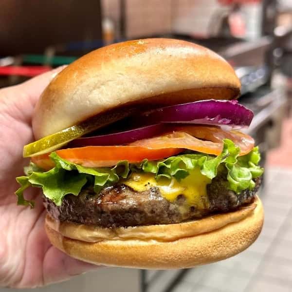 Classic cheeseburger stacked with melted cheddar, crisp lettuce, tomato, red onion, and pickles in a toasted brioche bun.