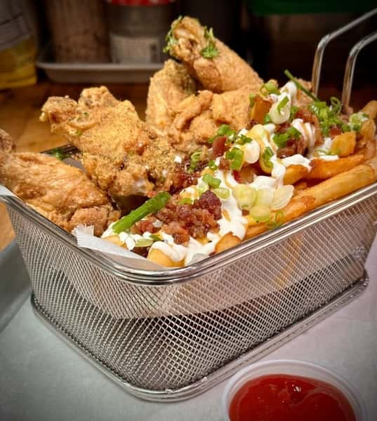 Basket of crispy fried chicken wings paired with loaded fries topped with bacon bits, scallions, and sour cream, served with a side of ketchup.