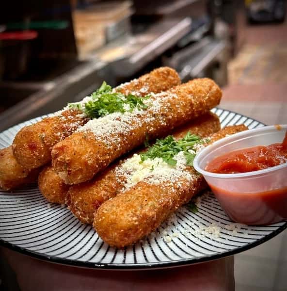 Crispy golden mozzarella sticks garnished with grated parmesan and parsley, served with a side of marinara sauce on a striped plate.