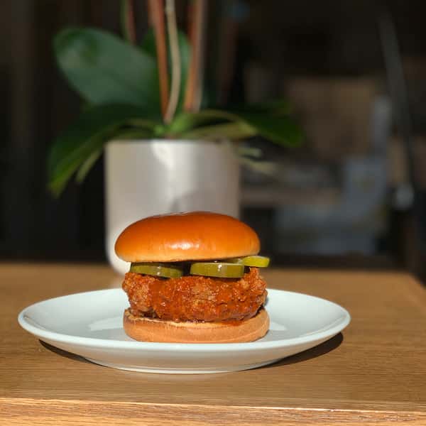 Nashville hot chicken sandwich featuring a spicy, crispy fried chicken breast topped with dill pickles on a toasted brioche bun, served on a white plate.