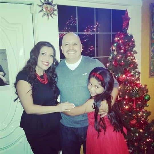 male, female, and young girl posing for picture with a christmas tree in the background