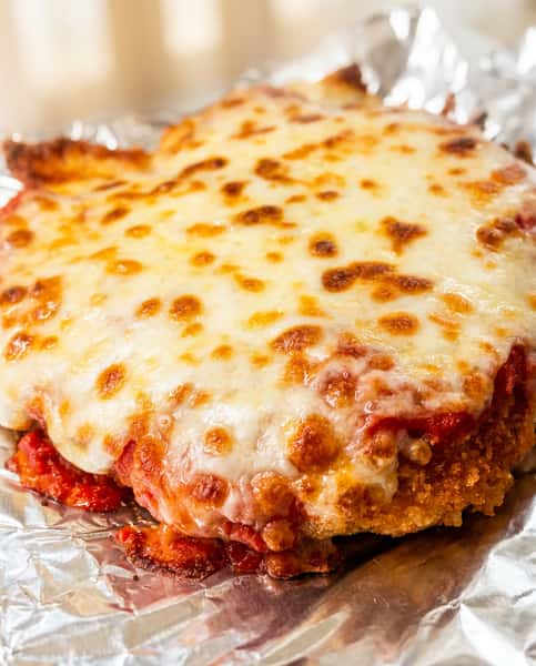 Breaded cutlet covered with melted, bubbly mozzarella cheese and red sauce, served on aluminum foil.