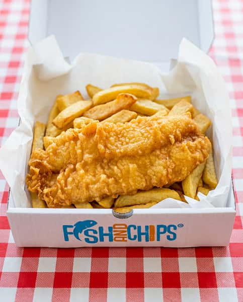 Fish and chips in a paper-lined cardboard box, with a red and white checkered tablecloth in the background.