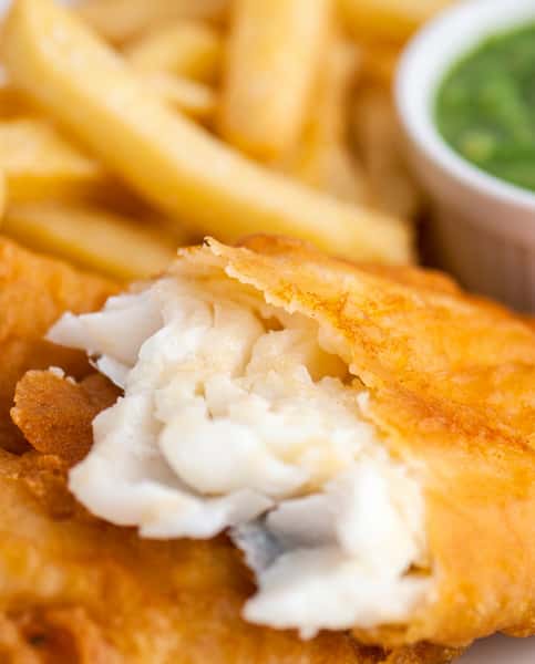 Fish and chips: flaky white fish in golden batter, with fries and a side of green sauce.
