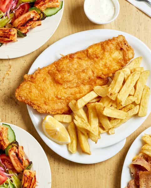 Fried fish and chips with a lemon wedge, kebab meat and fries, and grilled chicken with salad.