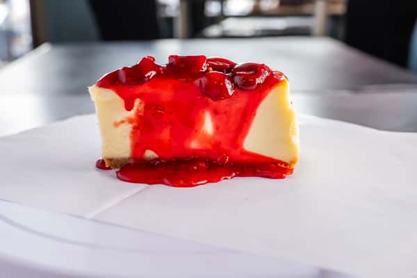 creamy cheesecake slice topped with glossy strawberry sauce and fresh berries, served as a classic dessert in restaurant setting