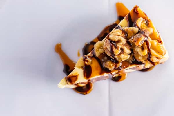 slice of cheesecake topped with walnuts and drizzled caramel and chocolate sauce, rich dessert presentation