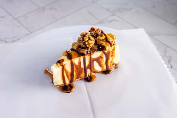 slice of cheesecake topped with walnuts and drizzled caramel and chocolate sauce, rich dessert presentation