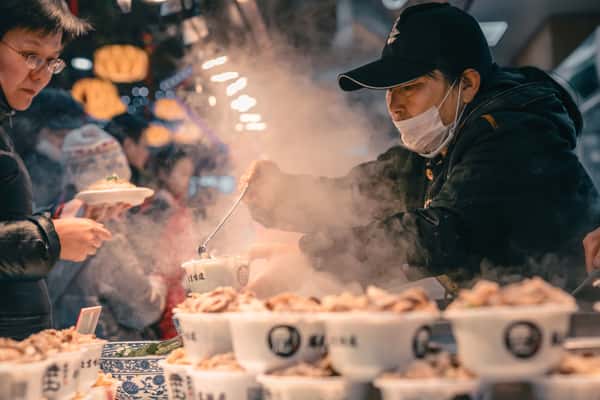 man pouring soup into a bowl at a night market