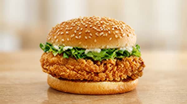 Crispy chicken sandwich with lettuce, white sauce, and a sesame seed bun.