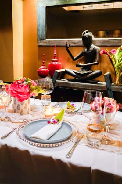 elegant restaurant dining table with floral centerpieces, candles, and Thai-inspired decor featuring a serene statue backdrop