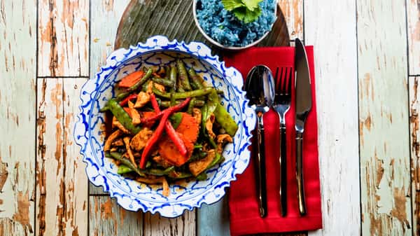 Thai stir-fried chicken with green beans and red peppers served with blue jasmine rice on a rustic table