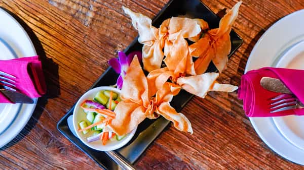 Crispy fried wonton appetizers served with sweet chili dipping sauce and fresh cucumber relish on a rustic wooden table