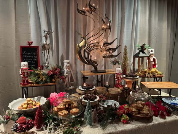festive dessert display with assorted pastries, macarons, and cakes on decorative stands, surrounded by holiday décor and candles in a cozy restaurant setting