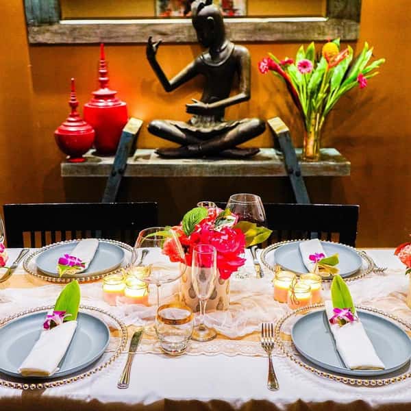 elegant restaurant dining table with floral centerpieces, candles, and Thai-inspired decor featuring a serene statue backdrop