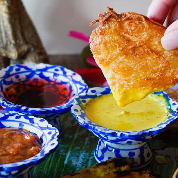 Crispy Thai roti dipped in creamy yellow curry sauce with traditional sweet and spicy dipping sauces on a banana leaf plate