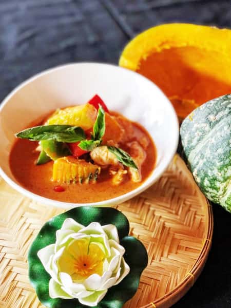 Thai red curry with pumpkin, vegetables, and basil served in a white bowl with fresh herbs and decorative garnish