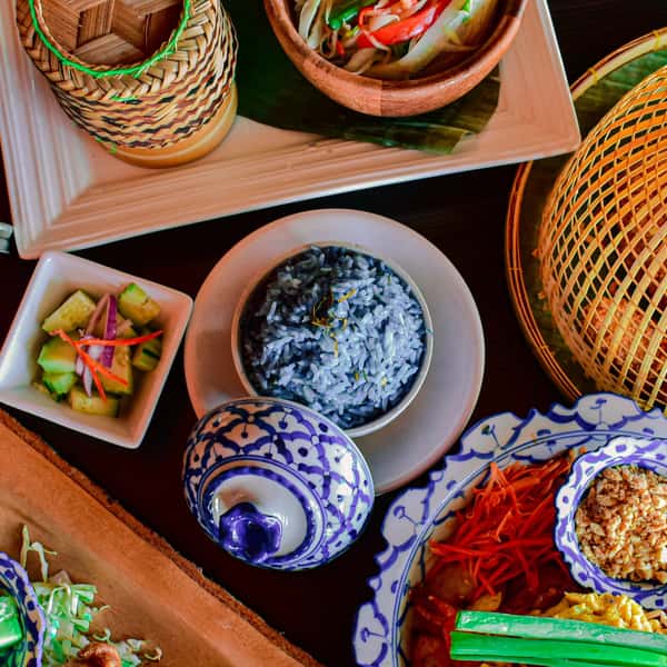 top view of Thai cuisine spread with blue rice, fresh vegetable sides, and traditional dishes served in ceramic bowls and woven baskets