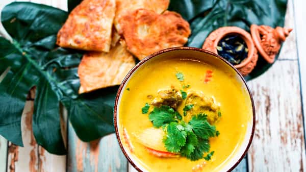 Thai yellow curry with tender chicken, potatoes, and coconut milk garnished with cilantro, served with roti bread