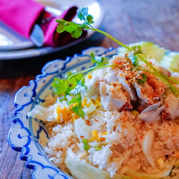 Thai crab fried rice topped with fresh cilantro, garlic, and chunks of crab meat served in a decorative blue bowl