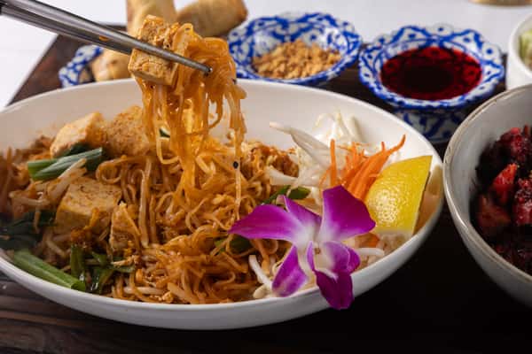 Authentic Thai noodles stir-fried in savory house-made sauce with fresh vegetables and aromatic seasonings, served with crispy spring rolls and vibrant traditional garnishes for a bold and satisfying flavor experience.