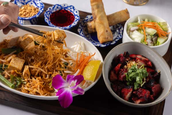 Classic Pad Thai stir-fried with tender noodles, fresh vegetables, and savory sauce, served with crispy spring rolls and flavorful Thai side dishes.