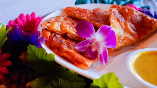 Crispy Thai roti flatbread served with sweet dipping sauce and garnished with fresh orchid flowers
