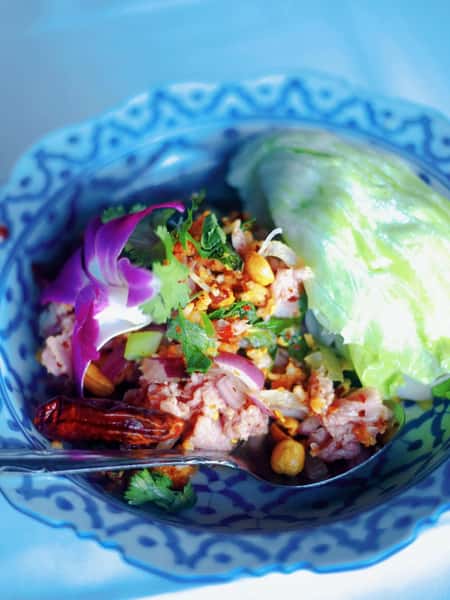Thai larb salad with minced meat, red onion, chili, cilantro, and toasted rice powder served with fresh cabbage in a decorative blue bowl