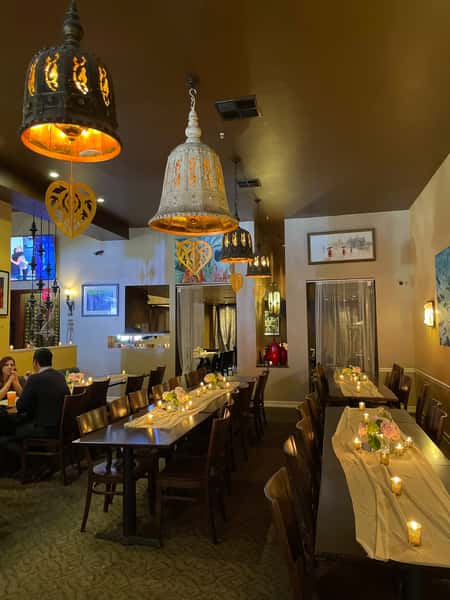 warmly lit Thai restaurant interior with candlelit tables, wooden seating, and decorative hanging lanterns creating an intimate dining atmosphere