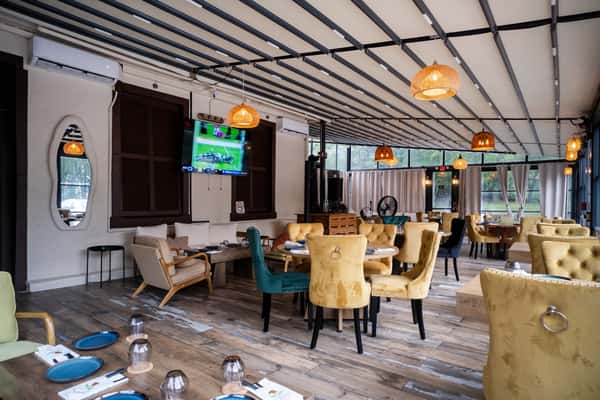 Bright patio dining area at Sivas Tavern with yellow chairs, TV screens, and modern decor