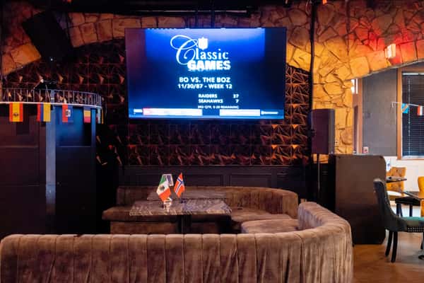 Dimly lit lounge area at Sivas Tavern featuring a large LED screen and curved sectional seating