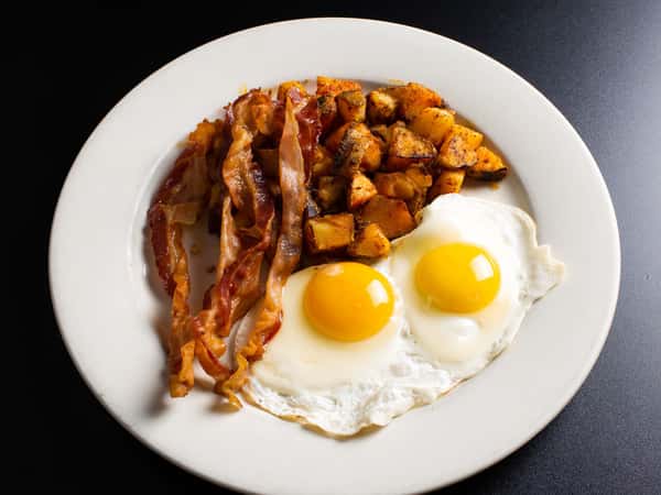 Two fried eggs sunny side up with bacon and potatoes