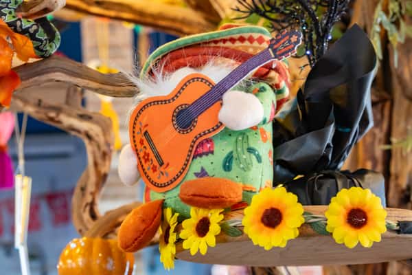 Festive plush doll wearing a sombrero and holding a guitar, surrounded by sunflowers and colorful decorations.