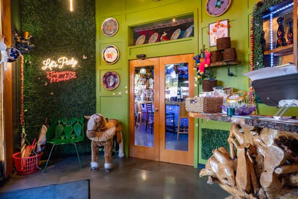 Colorful restaurant entrance with a neon "Let's Party I Taquero Mucho" sign, decorative plates, plush toys, and a small toy horse.
