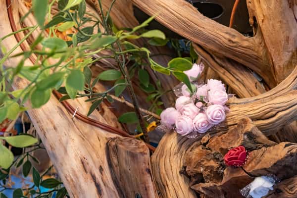 Close-up of a wooden branch arrangement decorated with small pink and red artificial roses and green leaves.