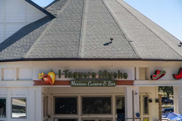 Exterior of I Taquero Mucho Mexican Cuisine & Bar with a large shingled roof and colorful signage featuring peppers and sombreros.