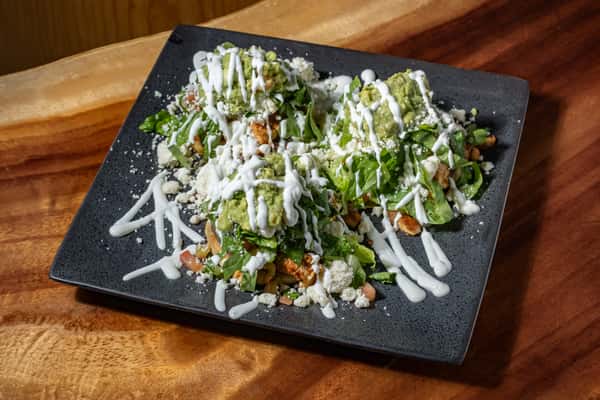 Tostadas topped with lettuce, guacamole, crema drizzle, queso fresco, and diced chicken on a black plate.