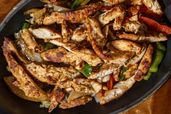 A sizzling skillet of grilled chicken fajitas, featuring tender strips of seasoned chicken breast with sautéed bell peppers and onions, cooked to perfection for a smoky, flavorful dish.