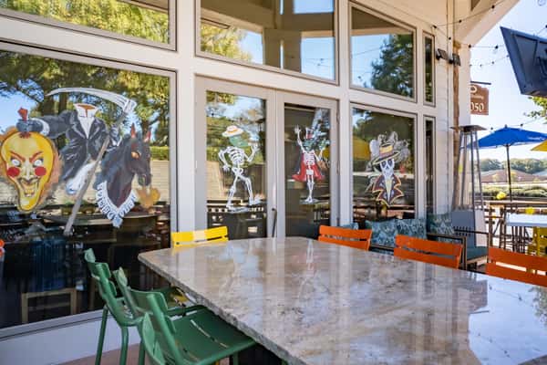 Large outdoor dining area with colorful chairs and tables, decorated with Halloween skeleton window art and bright umbrellas.