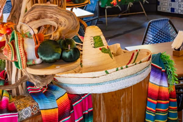 Colorful Mexican decor display featuring traditional sombreros, velvet peppers, and vibrant serape blankets on a wooden stand.