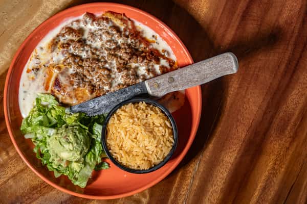 Plate of grilled chicken topped with creamy queso and seasoned beef, served with guacamole, lettuce, and Mexican rice.