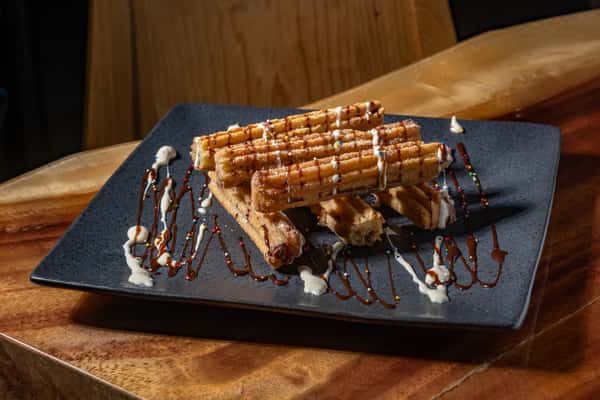 Plate of churros drizzled with chocolate and cream sauces, topped with colorful sprinkles for a festive dessert presentation.