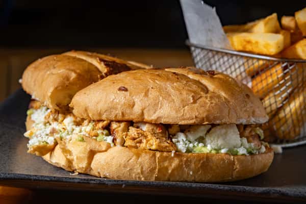 Mexican torta sandwich filled with seasoned meat, cheese, and avocado, served with a side of golden fries in a metal basket.