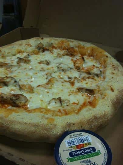 A round pizza with melted mozzarella and meat with a side of ranch dressing