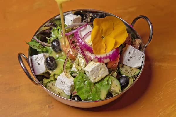 Greek salad being drizzled with dressing