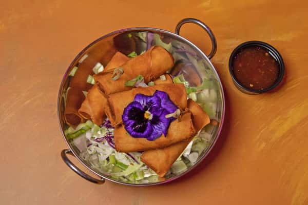 Shrimp spring rolls in a bowl with a purple flower garnish